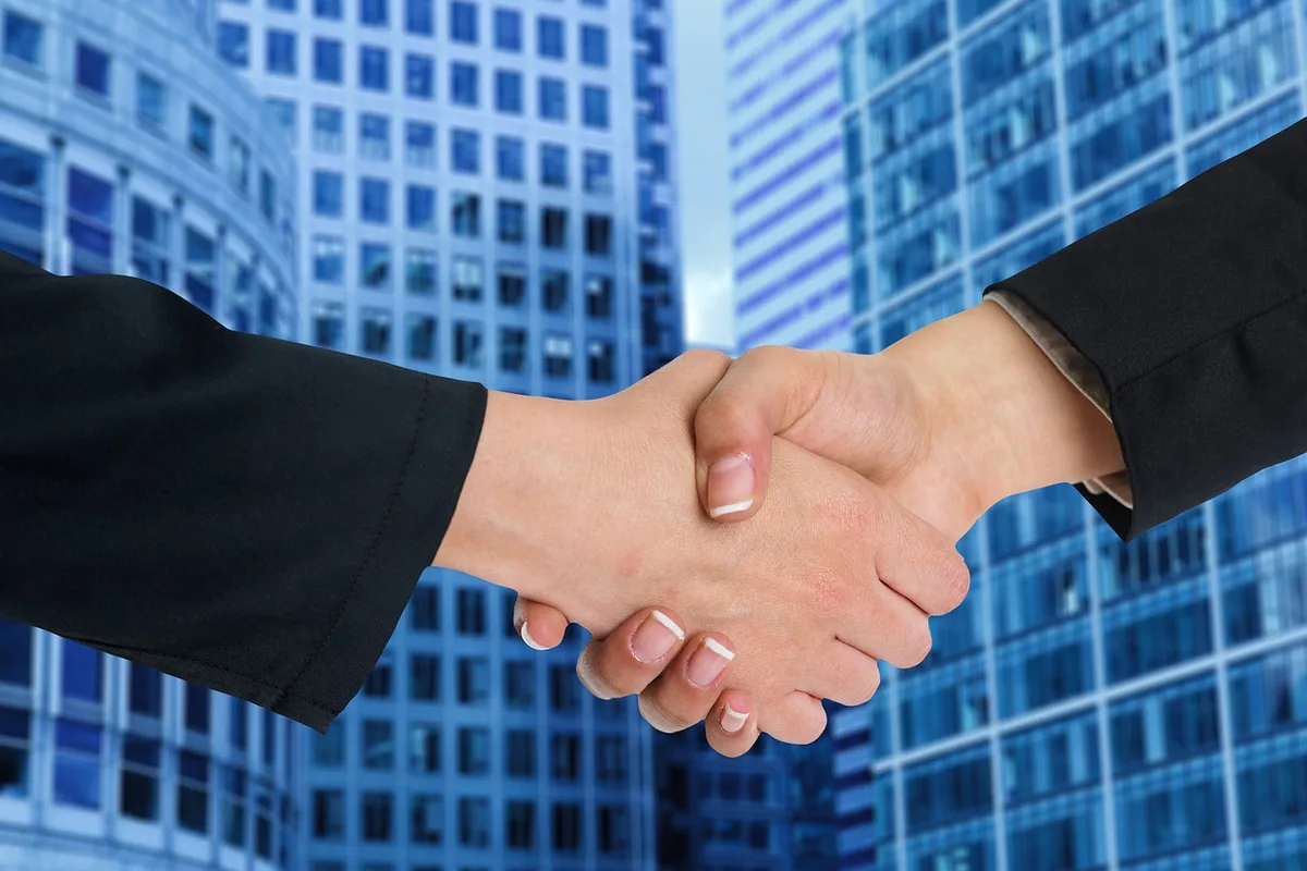 Two executives shaking hands over TV deal documents